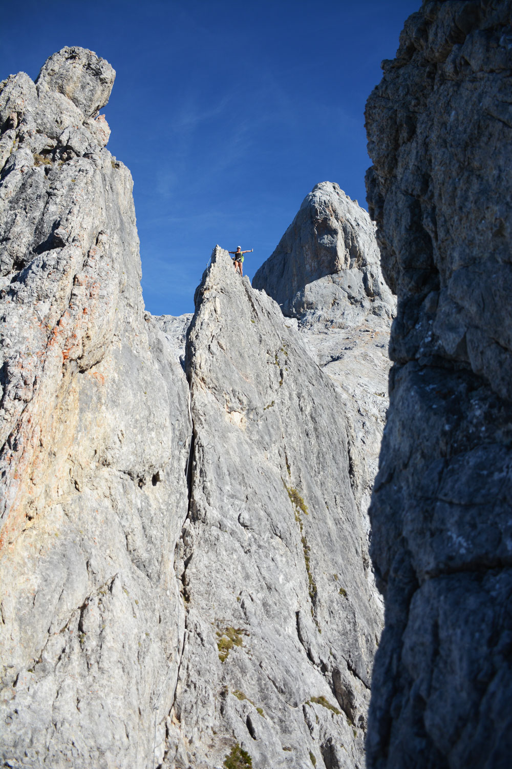 Massive Steilwand mit Felsspitzen, auf einer Spitze ist eine Person zu erkennen.