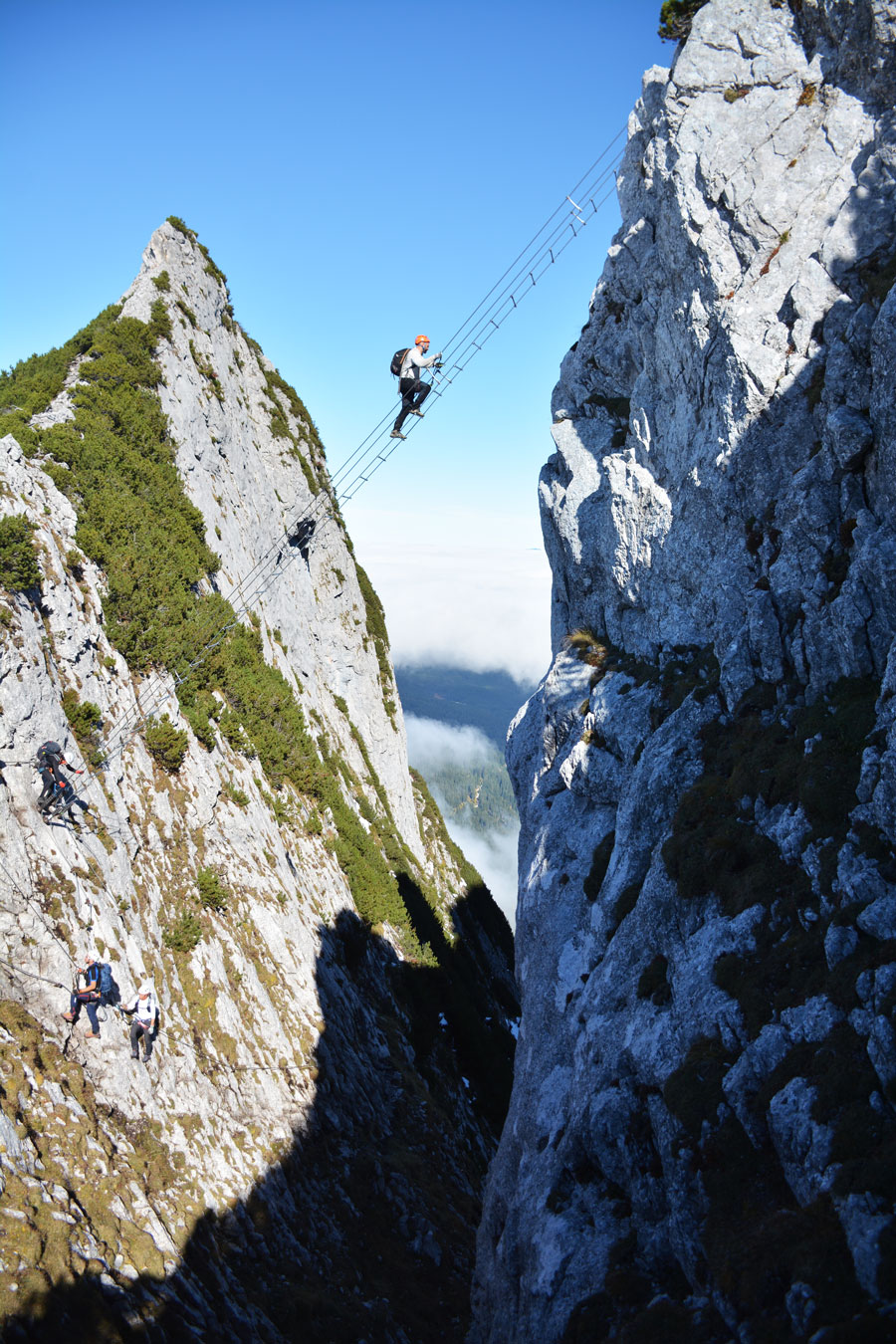 Eine kletternde Person auf einer Seilleiter, gespannt zwischen zwei Felswänden in luftiger Höhe