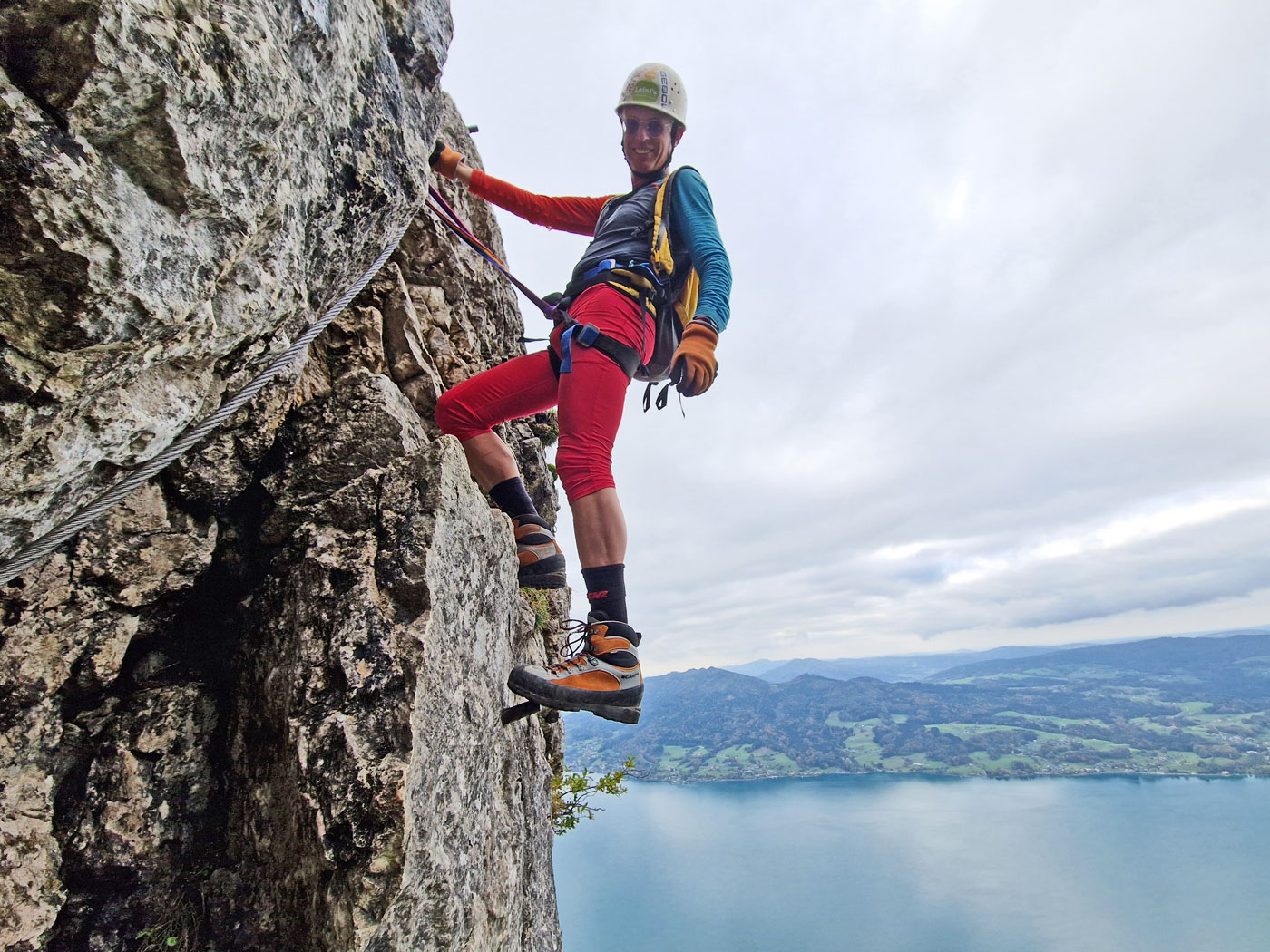 Mann im Klettersteig, unter ihm im Hintergrund ein blauer See