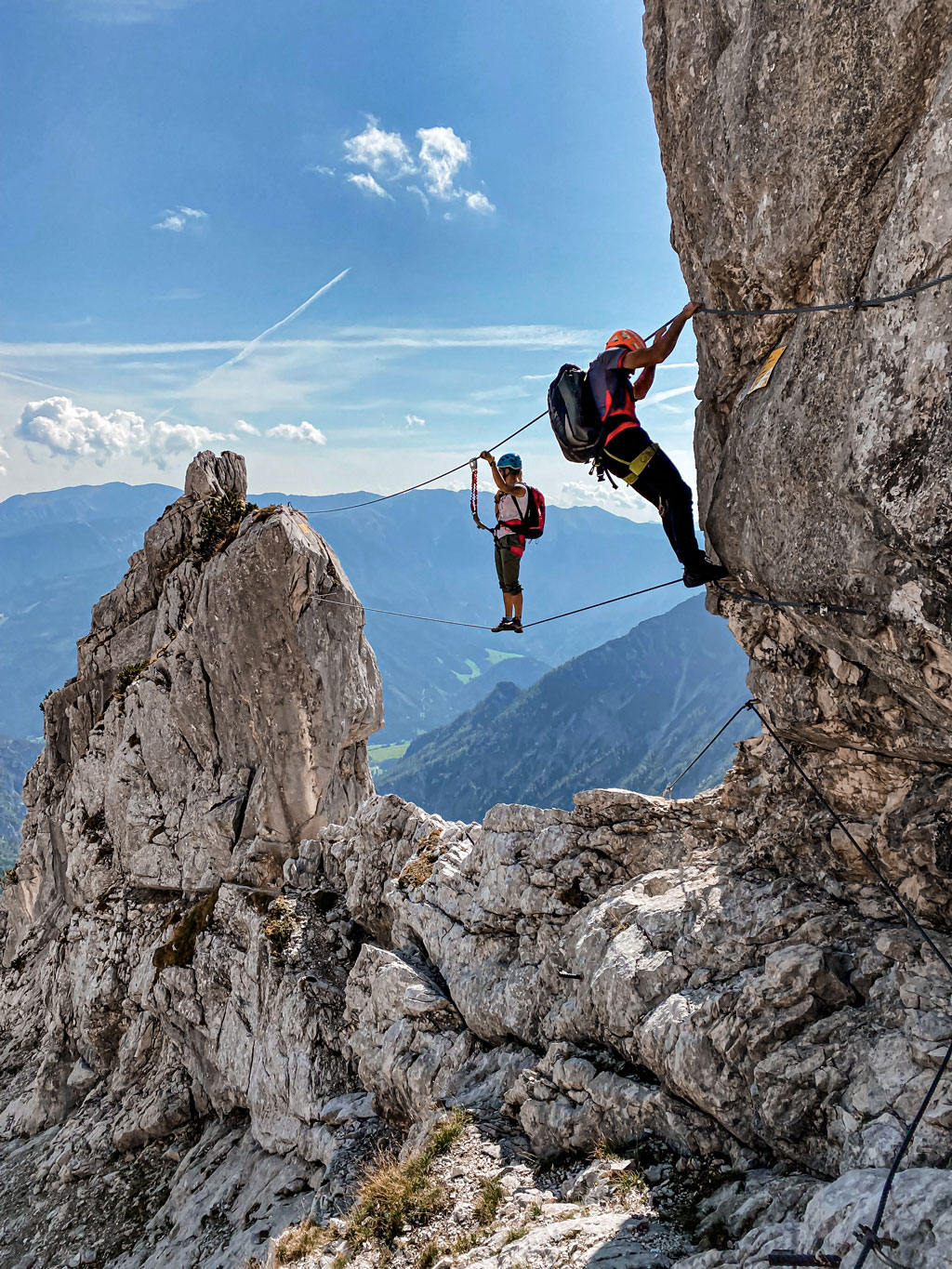 Zwei Personen stehen gesichert auf einem Seil zwischen zwei Felsspitzen.