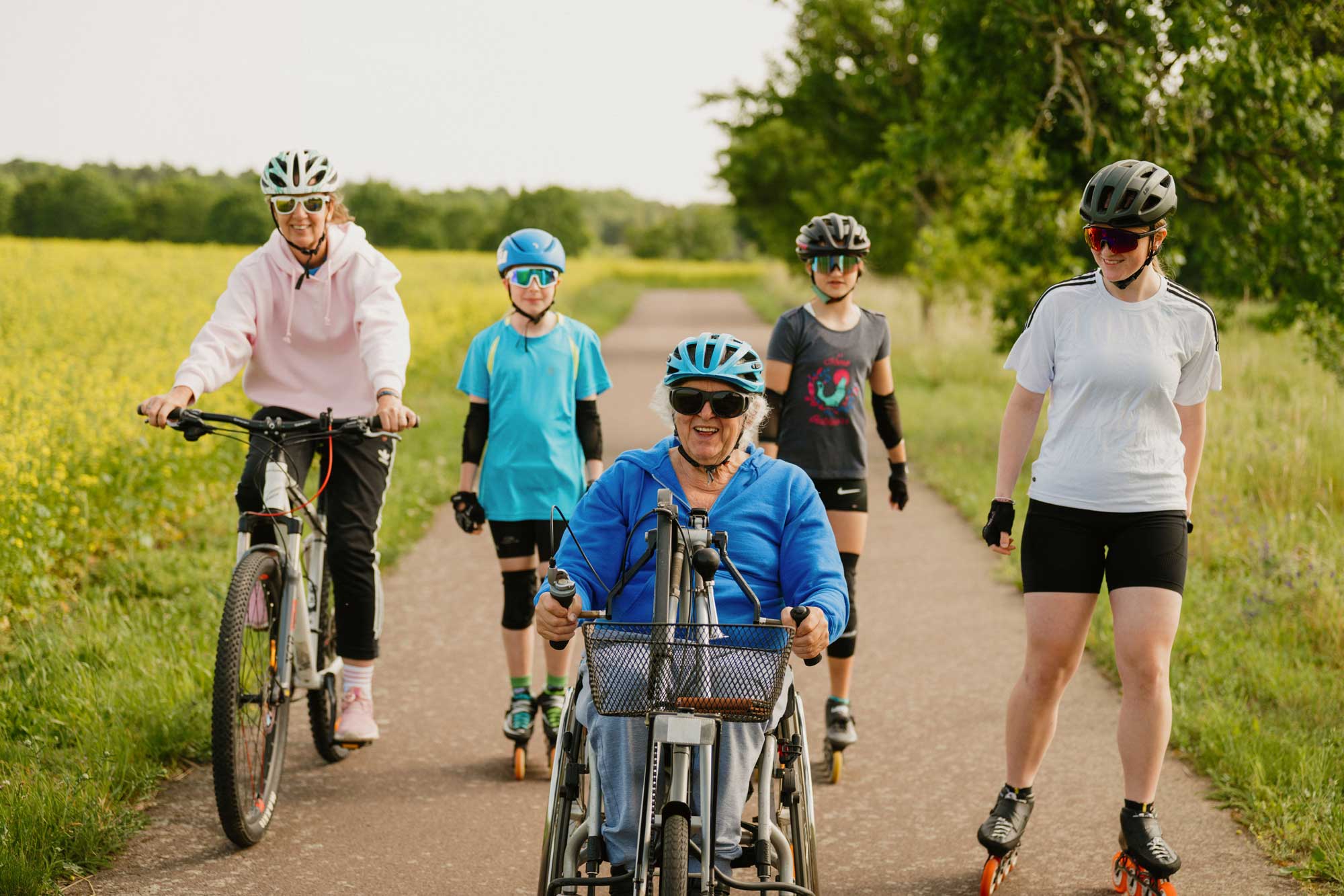 Eine Frau mit einem Rollstuhl, Kinder auf Inlinern und eine Frau auf einem Fahrrad