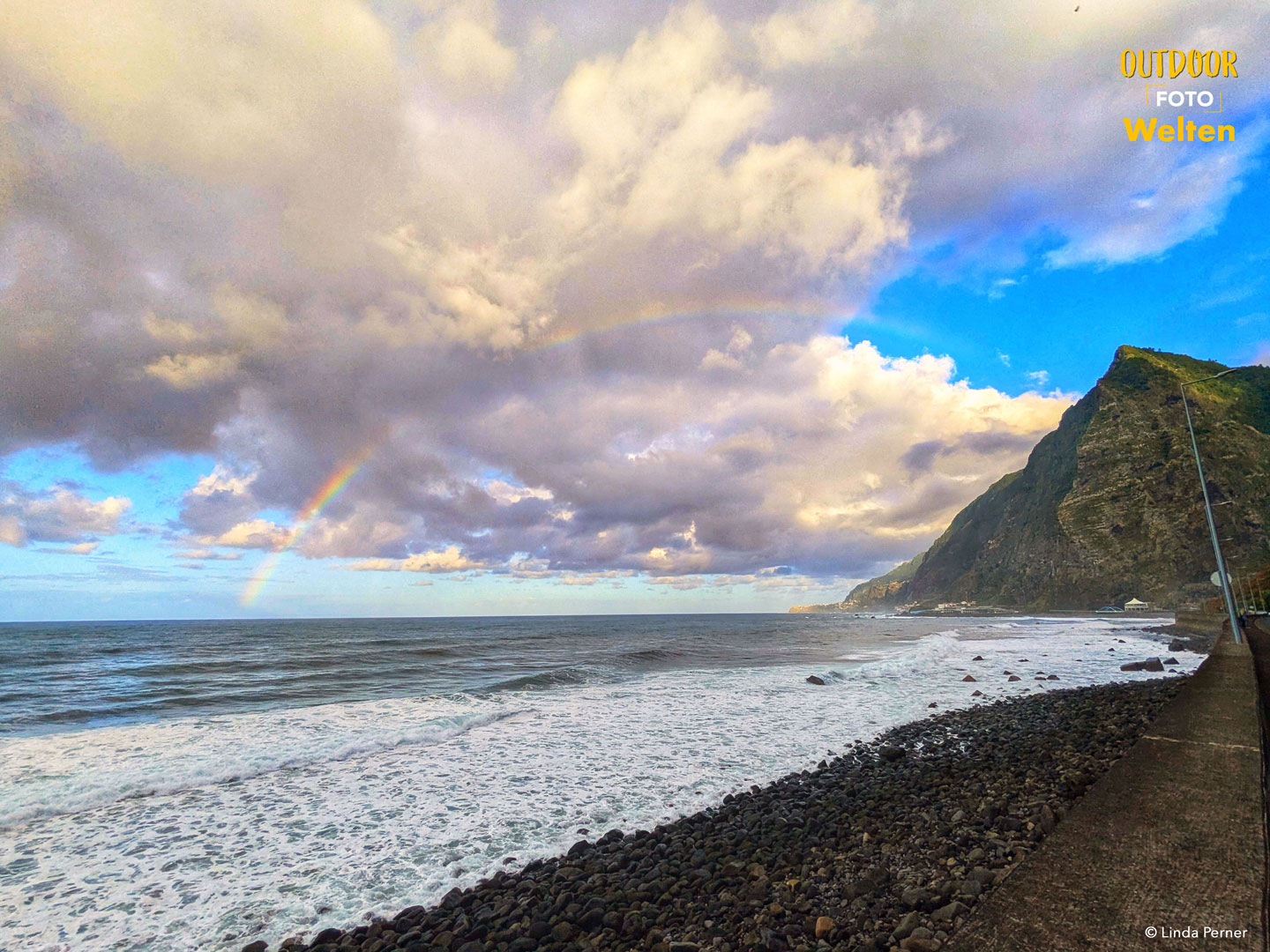 Ein Kiesstrand und die Küste mit einem Regenbogen