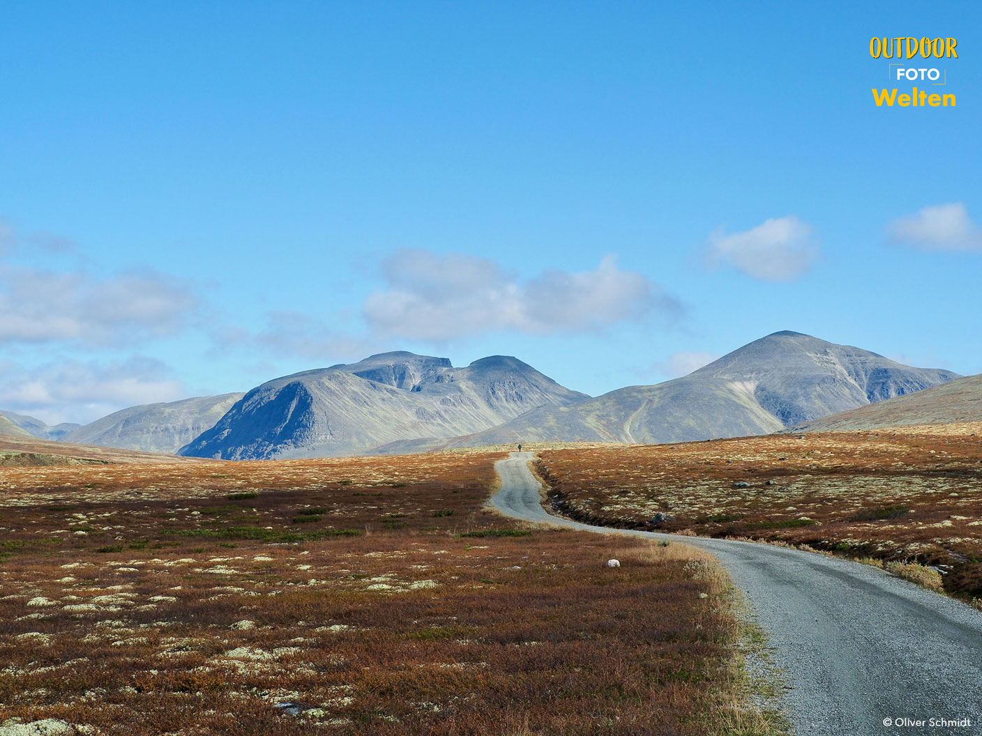 Eine Schotterstraße führt durch eine karge Landschaft auf ein Gebirgsmassiv zu.