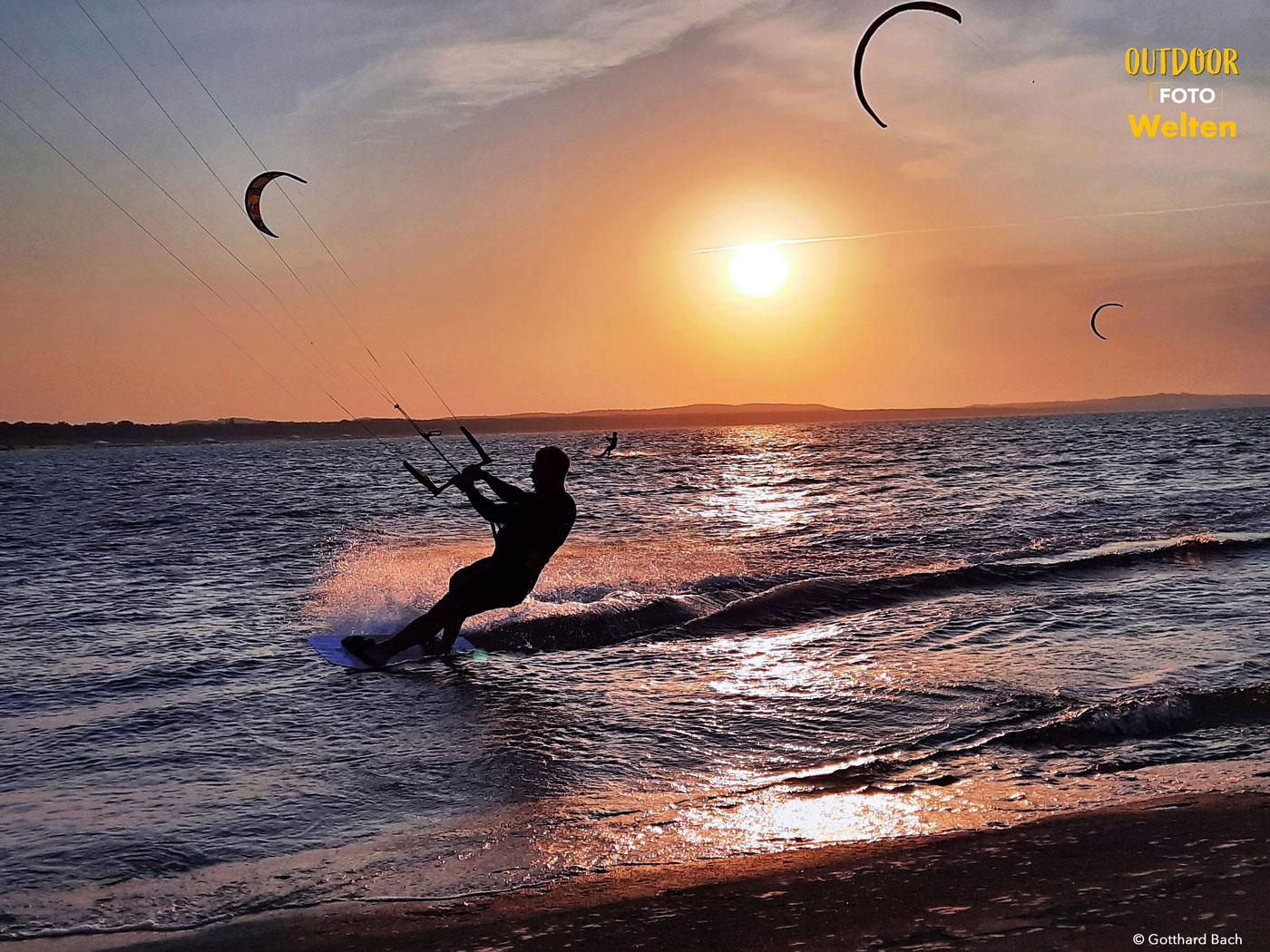 Die Silhouette eines Kitesurfers auf dem Wasser vor der untergehenden Sonne