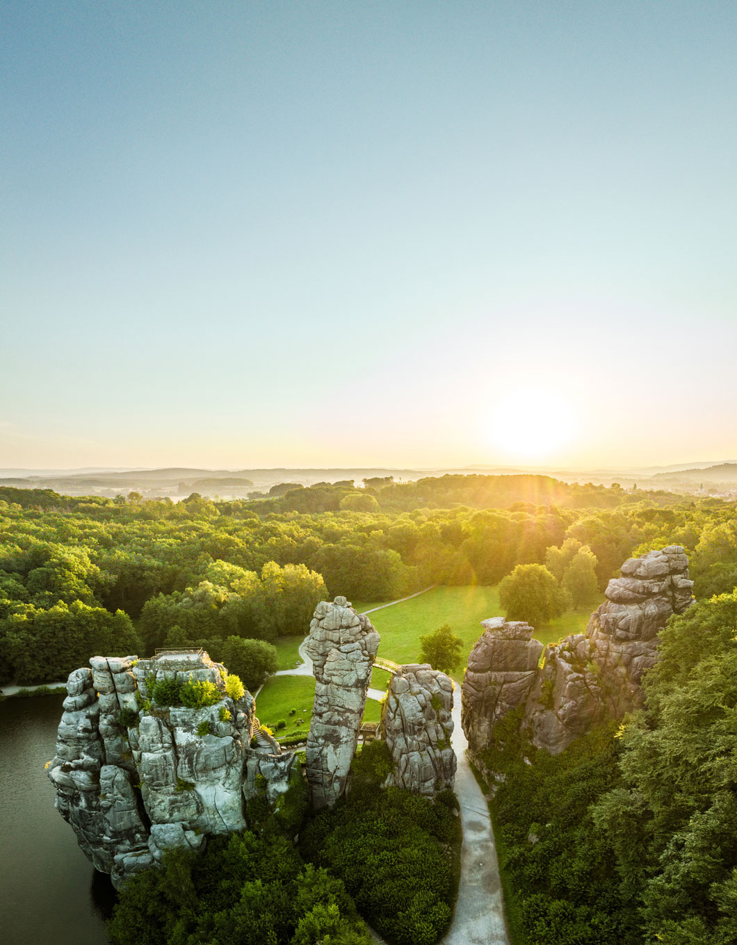 Markante Felstürme von oben im Sonnenlicht, im Hintergrund breitet sich eine Waldlandschaft und der Himmel aus.