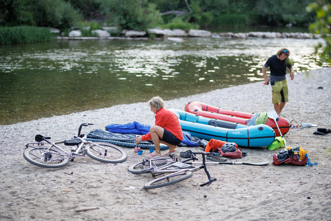 Eine Frau und ein Mann am Flussufer mit Packrafts und Fahrrädern