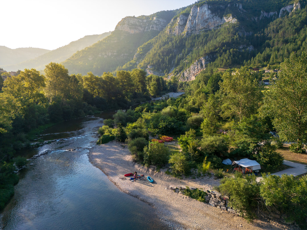 Luftaufnahme eines Flusses zwischen sattgrüne, bergigen Landschaft und steilen Felsen, am sandigen Ufer zwei Paddler mit ihren Booten