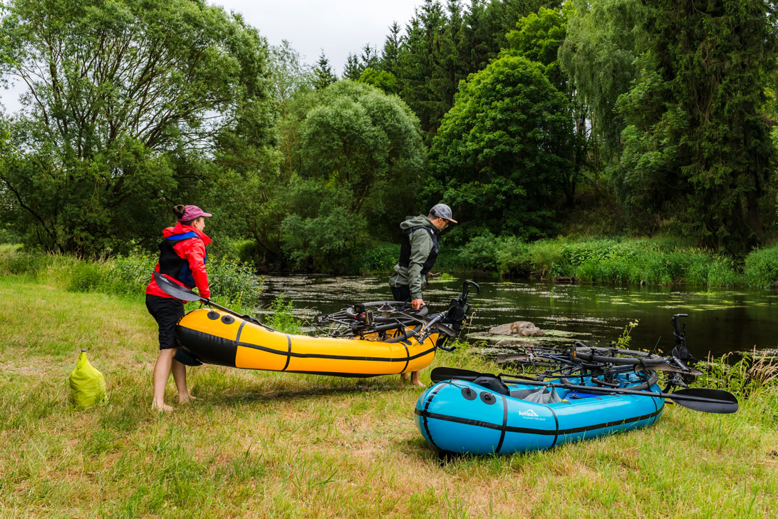 Zwei Personen tragen Packrafts zum Wasser