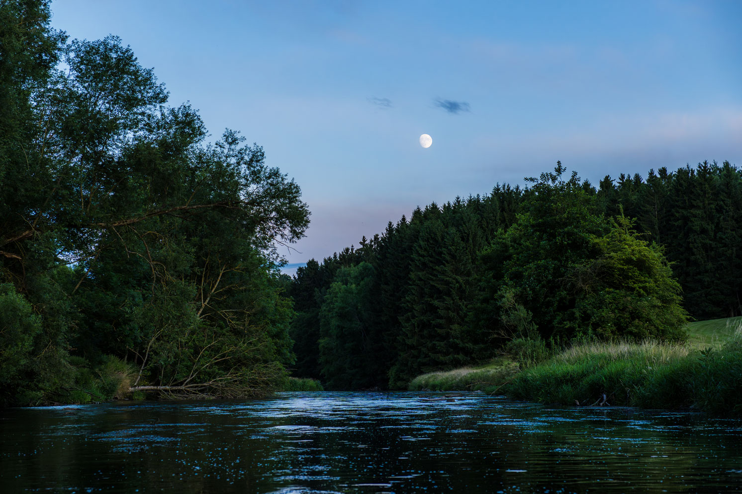 Ein Fluss im Abendlicht mit dem Mond am Himmel