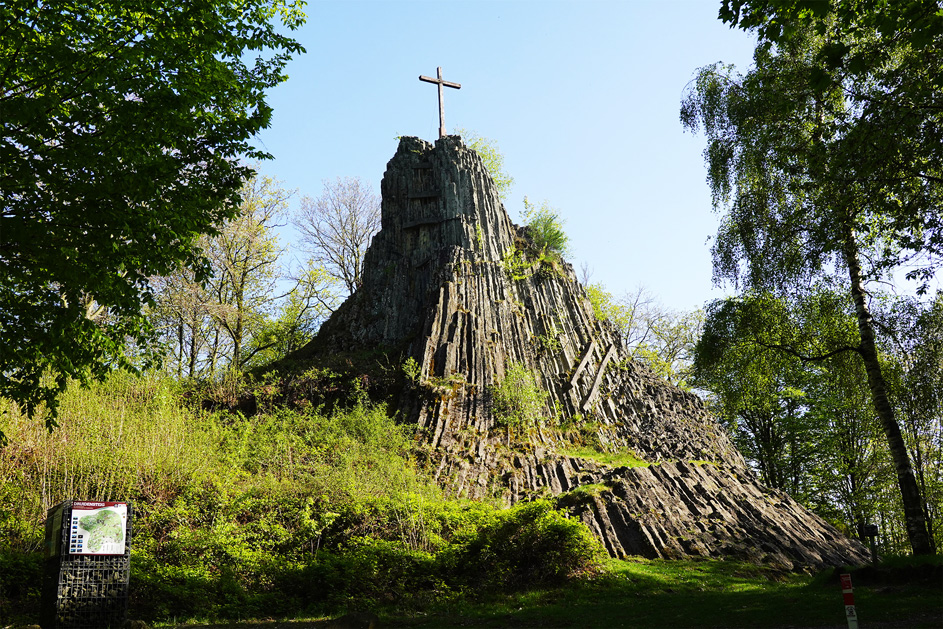 Ein pyramidenförmiger Fels mit Gipfelkreuz im Wald