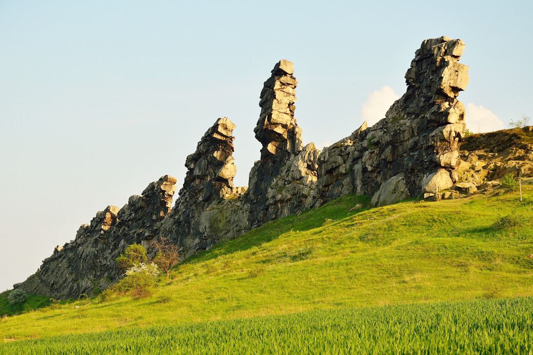Auf einem Wiesenhang thront eine Felsmauer mit hoch aufragenden Felstürmen